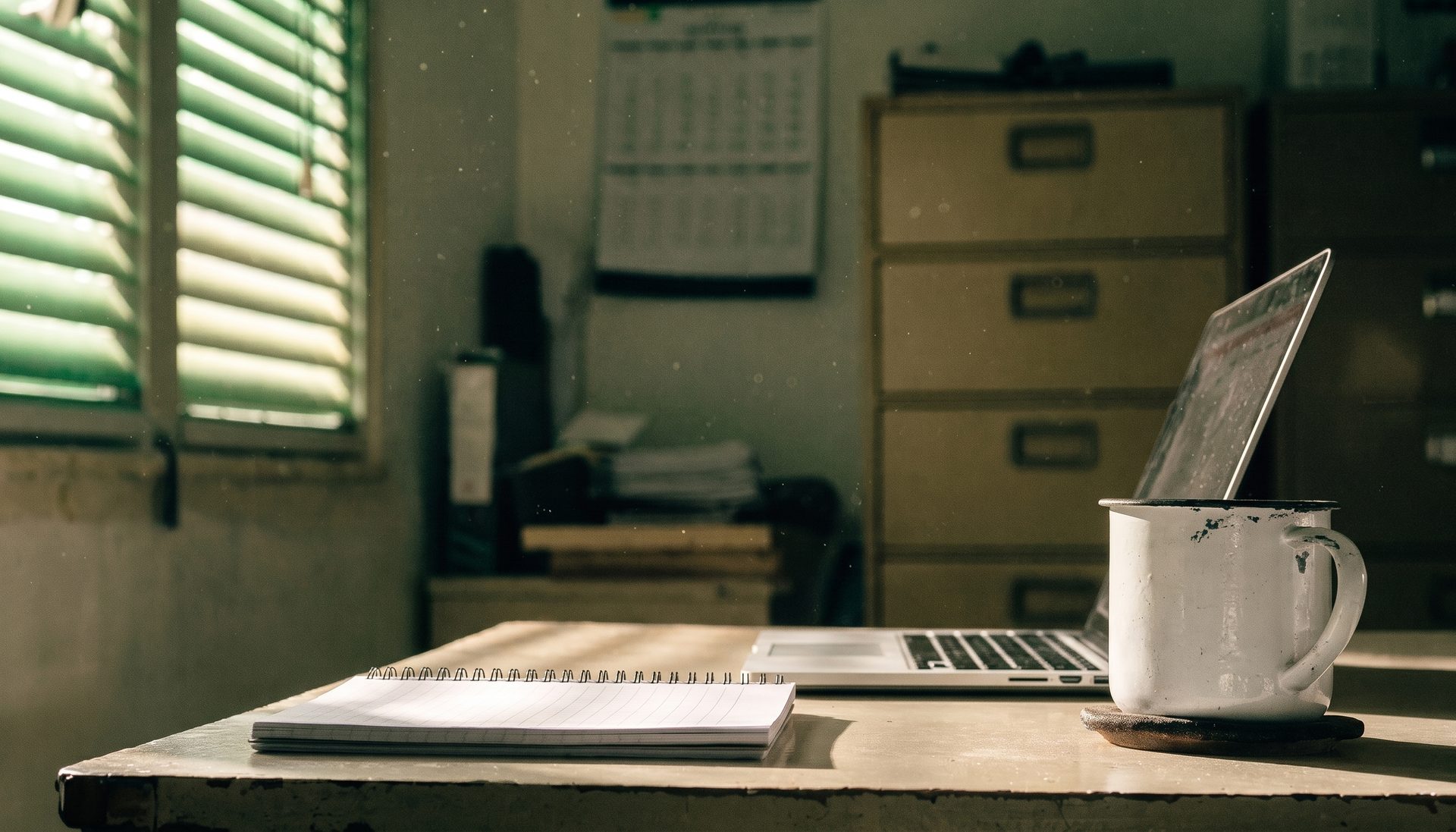 The same office desk, now clear, holding only an open laptop, a closed notebook and a mug.